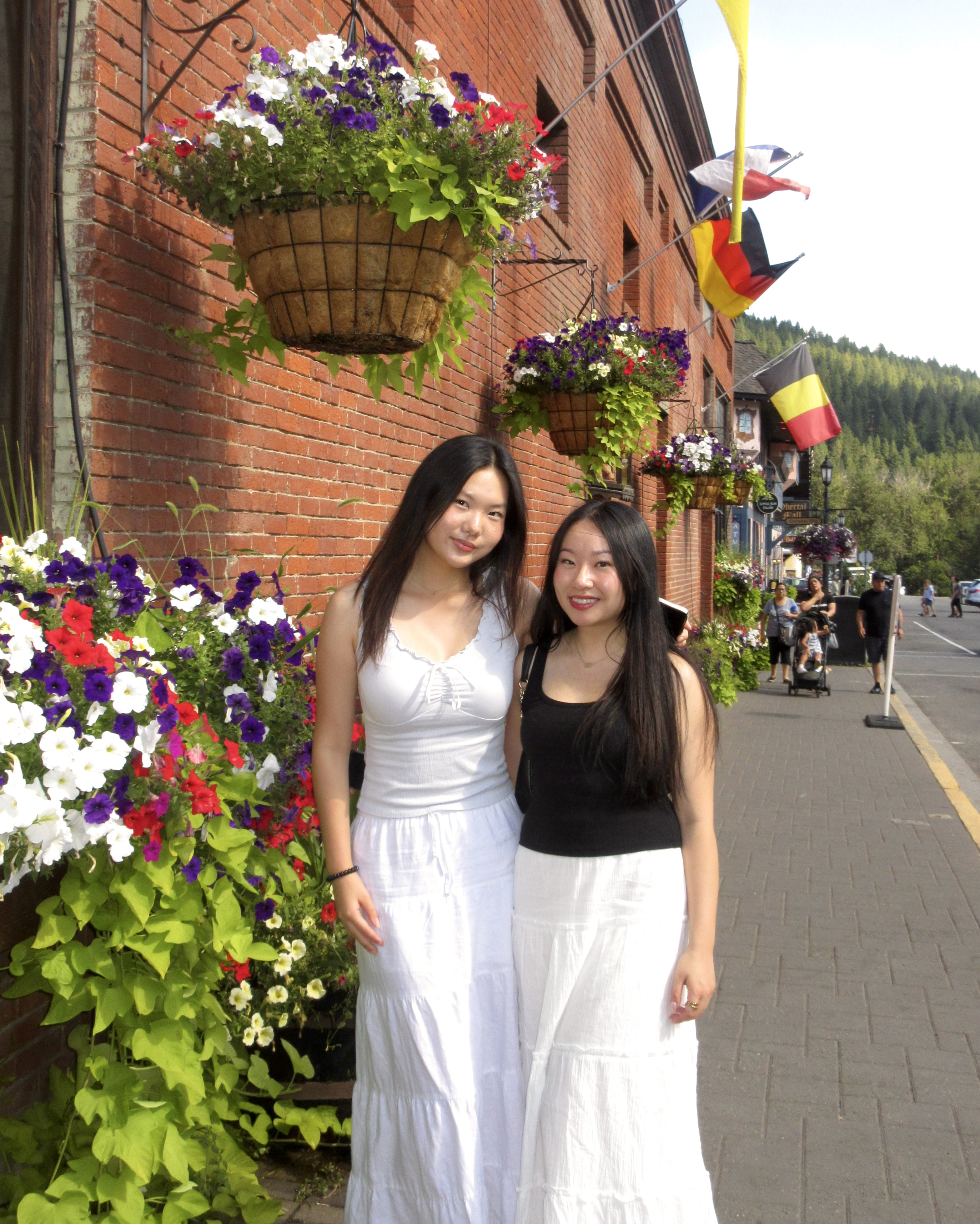 Tina and a friend standing in front of hanging flower baskets on a brick storefront.